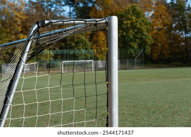 A soccer goalpost stands quietly on an empty field, surrounded by vibrant autumn foliage and clear skies, showcasing a tranquil daytime atmosphere. - Powered by Shutterstock