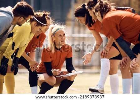 Soccer player and her teammates talking while analyzing tactics with their coach on playing field.