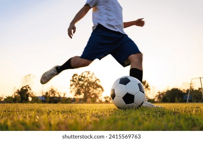 Soccer player kicking ball. Action sport outdoors playing football for exercise at green grass field under the twilight sunset. - Powered by Shutterstock