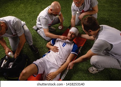 Soccer Player Received A Head Injury During The Game. Sport Doctors Provide First Aid To Player On A Professional Football Field