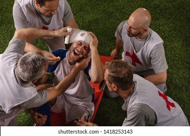 Soccer Player Received A Head Injury During The Game. Sport Doctors Provide First Aid To Player On A Professional Football Field