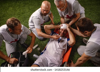 Soccer Player Received A Head Injury During The Game. Sport Doctors Provide First Aid To Player On A Professional Football Field