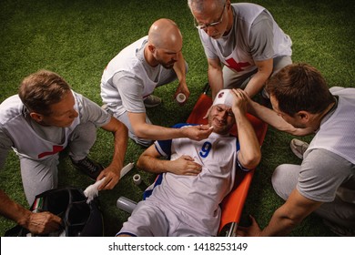 Soccer Player Received A Head Injury During The Game. Sport Doctors Provide First Aid To Player On A Professional Football Field