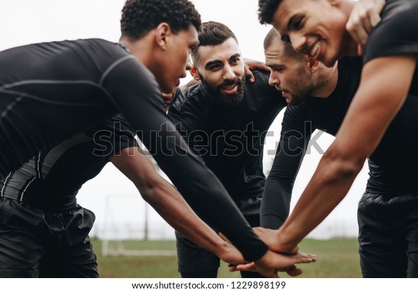 Soccer players joining hands in huddle talking\
about the game strategy. Low angle view of footballers bending\
forward in a huddle holding\
hands.