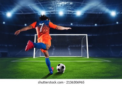 Soccer scene at night match with player in an orange and blue uniform kicking the penalty kick