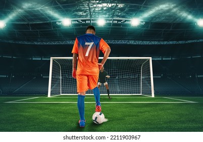 Soccer scene at night match with player in orange uniform kicking the penalty kick