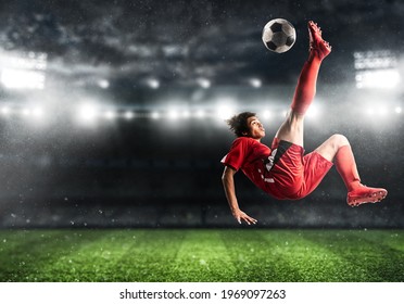 Soccer striker in red uniform hits the ball with an acrobatic kick in the air at the stadium