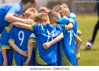 The soccer team huddles in a circle with a coach during the time break. Kids on the football team stand united and listen to the coach's motivational speech. Sporty children in blue soccer uniforms - Powered by Shutterstock