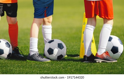 Soccer Training Class. Legs Of Children On Football Lesson. Kids Practicing Soccer Skills On School Grass Field. Boys Standing Next To Yellow Training Cone In A Row