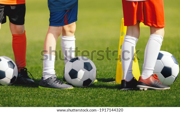Soccer Training Class.\
Legs of Children on Football Lesson. Kids Practicing Soccer Skills\
on School Grass Field. Boys Standing Next to Yellow Training Cone\
in a Row