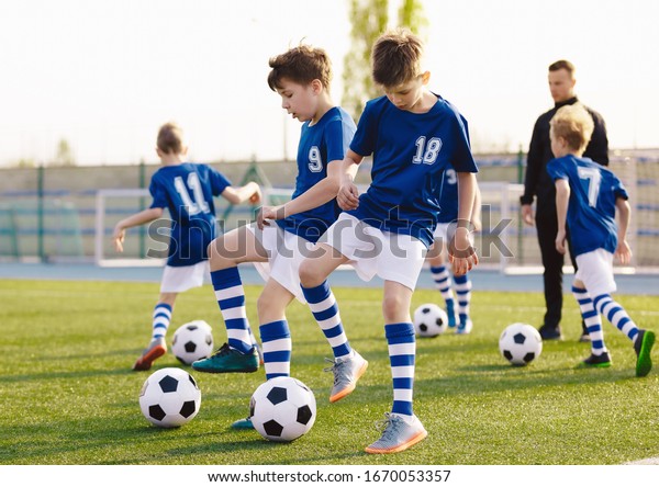 Soccer Training Exercises for Kids. Boys\
Training with Balls on Summer Football Grass Field. Young Sporty\
Kids in a Team with Coach. Practice Soccer Unit for School\
Children. Stadium in the\
Background