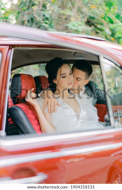 SOCHI, RUSSIA NOVEMBER 16, 2019: Gorgeous wedding\
couple. Wedding for two. Husband and wife are sitting and hugs\
inside a red retro car.
