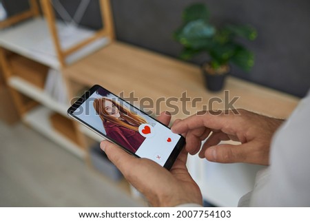 Social app for searching for romantic partner. Close up of male finger reaching for heart button on screen in online dating app on mobile smartphone. Online dating concept.