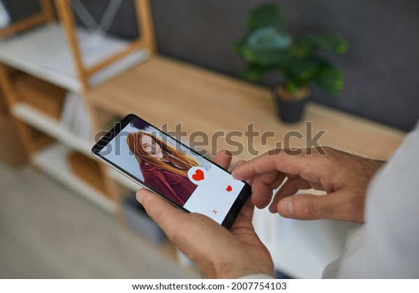 Social app for\
searching for romantic partner. Close up of male finger reaching\
for heart button on screen in online dating app on mobile\
smartphone. Online dating\
concept.