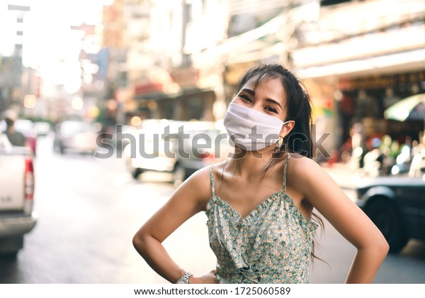 Social distance and new normal lifestyle virus\
protect at outdoor area concept. Happy asian adult woman tan skin\
wear mask on face. Background chinatown landmark destination.\
Bangkok, Thailand.
