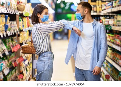 Social Distance In Supermarket. Woman In Protective Mask Bumping Elbows With Guy Meeting Him Doing Grocery Shopping Walking Along Aisle In Food Store. Shop Safe During Covid-19 Coronavirus Pandemic