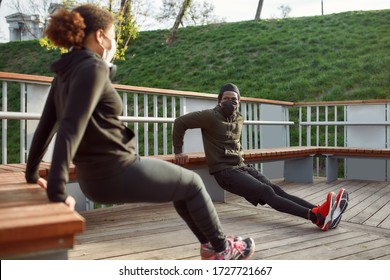 Social distancing. African couple in protective masks working out in park outdoors. Doing push-ups exercises on bench, training triceps. Sport in quarantine. Covid-19. Protection - Powered by Shutterstock