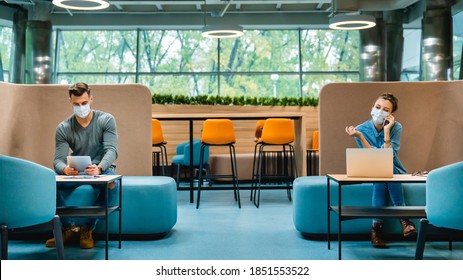 Social Distancing Concept. Two Colleagues Sitting In 1.5 Metres Distance In Medical Masks Against Covid19 In Modern Office