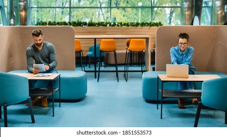 Social Distancing Concept. Two Colleagues Sitting In 1.5 Metres Distance In Medical Masks Against Covid19 In Modern Office. Horizontal Shot