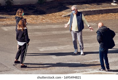Social Distancing, Coronavirus Lockdown: Hugging At Risk Of Infection For Worried Old Man And Young Women (All Wearing Face Masks) Gathering In The Street In Covid-19 Quarantine. Symbolic. April 2020