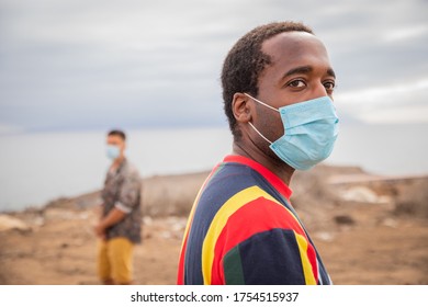 Social Distancing During Coronavirus Pandemic  Two Boys, Black And White Males, Stand Far Apart And Wear Surgical Masks To Avoid The Risk Of Getting Infected From Covid-19. Social Distance Concept