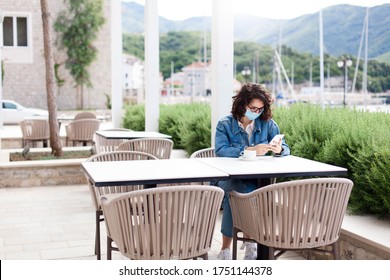 Social Distancing During Quarantine. Young Woman Wearing Protective Mask In Empty Cafe Outdoors. Girl Using Mobile Phone. Lifestyle Moment In New Normal. Restaurant Terrace With Safety Limited Seating