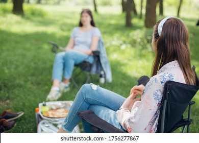 Social Distancing. Girls Friends Chilling Among Trees At Picnic With Social Distance In Summer Park. Leisure Activity Together In New Normal, Safety Gatherings. Young Woman Relaxing