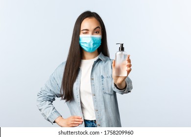 Social Distancing Lifestyle, Covid-19 Pandemic Preventing Virus Concept. Cheerful Asian Woman In Medical Mask Wink, Encourage People Use Hand Sanitizer And Wash Hands During Coronavirus