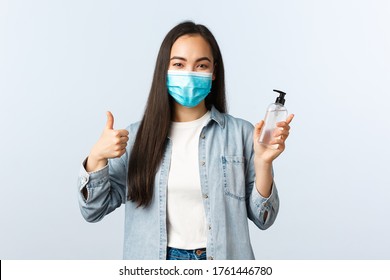 Social distancing lifestyle, covid-19 pandemic preventing virus concept. Cheerful asian woman in medical mask show thumb-up, encourage people use hand sanitizer and wash hands during coronavirus - Powered by Shutterstock