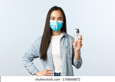 Social distancing lifestyle, covid-19 pandemic preventing virus concept. Young cute asian female in medical mask advice using hand sanitizer, showing soap bottle, explain measures during coronavirus - Powered by Shutterstock