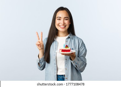 Social distancing lifestyle, covid-19 pandemic, celebrating holidays during coronavirus concept. Happy smiling asian birthday girl holding bday cake and show peace sign