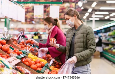 Social distancing in a supermarket. A young woman in a disposable face mask buying fruits and vegetables and putting them in a grocery basket. Shopping during the Coronavirus Covid-19 epidemic 2020