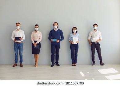 Social Distancing At Work Concept. Office Workers Or Job Candidates In Protective Face Masks Standing In Corridor. Applicants Waiting For Interview Keeping Safe Distance To Prevent Spread Of Covid 19