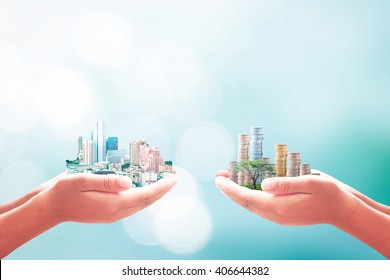 Social Entrepreneurship Concept: Two Human Hand Holding Big City And Coins Over Blurred Blue Nature Background.