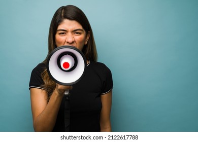 Social injustice. Angry latin woman using a megaphone to give a loud message or announcement - Shutterstock ID 2122617788