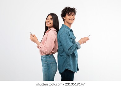 Social Media Application. Smiling Young Couple Using Smartphones Posing Standing Back To Back On White Studio Background. Youth Texting And Surfing Web Via Phones Advertising Mobile Offer - Powered by Shutterstock