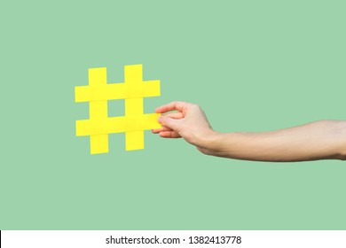 Social Media Concept, Closeup Portrait Of Hand Holding Large Big Yellow Hash Tag Sign. Indoor, Isolated, Copy Space, Green Background, Marketing Symbol, Instagram Followers