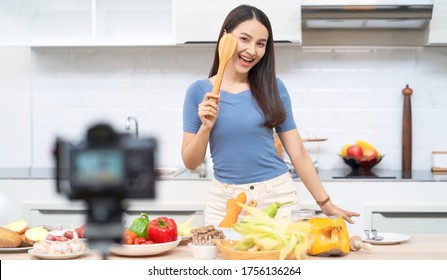 Social media concept. Happy woman standing in kitchen, using camera and recording online video. Happy asian woman vlogger broadcasting live video online teaching cooking food in kitchen at home - Powered by Shutterstock