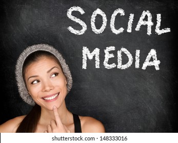 Social Media Concept With University Student Looking Thinking At SOCIAL MEDIA Text On Blackboard. Female College Student Girl In Front Of Black Chalkboard. Trendy Cool Multiracial Asian Caucasian Girl