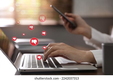 Social media dislike reaction. Woman using laptop and mobile phone at table, closeup. Thumbs down illustrations over device