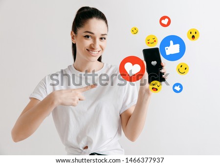Social media interactions on mobile phone. Internet digital marketing, Chating, commenting, liking. Smiles and icons above smartphone screen, that holding by young woman on white studio background.