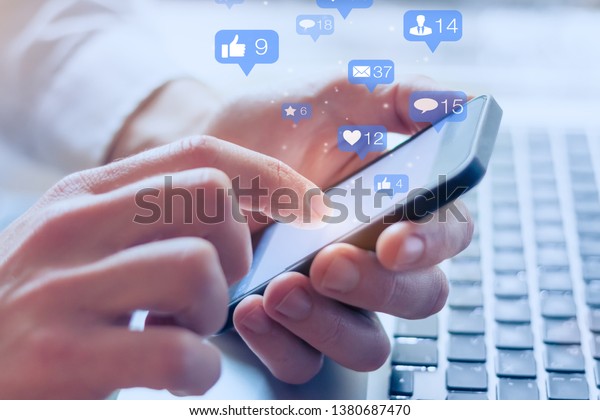 Social media interactions on mobile phone,\
concept with notification icons of like, message, email, comment\
and star above smartphone screen, person hands holding device,\
internet digital\
marketing