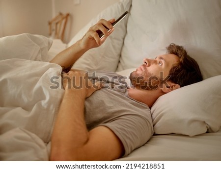 Social media, mobile app and relax man with smartphone using the internet or online website content at night in his bedroom with home wifi. Serious insomnia person reading blog for sleep health tips