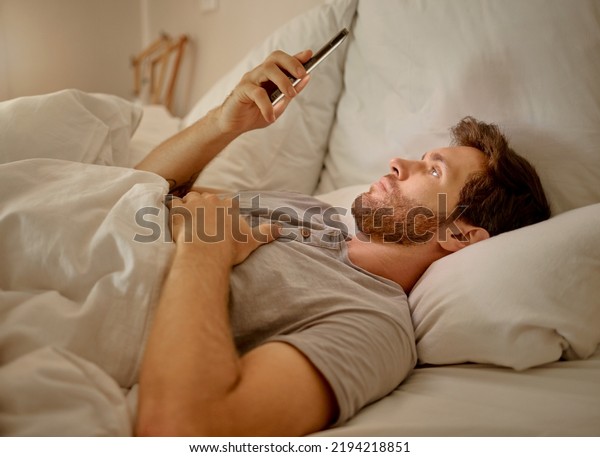 Social media, mobile app and relax man with\
smartphone using the internet or online website content at night in\
his bedroom with home wifi. Serious insomnia person reading blog\
for sleep health tips