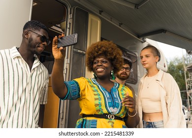 Social Media Personality - Beautiful Positive Black Woman In Her Late 20s Wearing Yellow And Blue Dress Smiling At Her Smartphone And Recording Her Multiracial Friends During Camping. Summertime