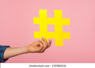 Social media trends. Closeup of female hand holding yellow hashtag sign, sharing tagged message, famous internet post, blogging and viral content. indoor studio shot isolated on pink background