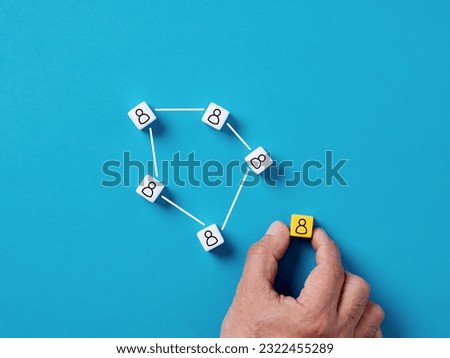 Social networking or organizational network. Team building. Adding a new member to the team. Assigning the team leader. Male hand places a cube with person symbol next to the network of people.