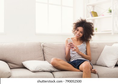 Social Networks. Young Black Woman Messaging On Smartphone At Home, Sitting Comfortably On Beige Sofa, Copy Space