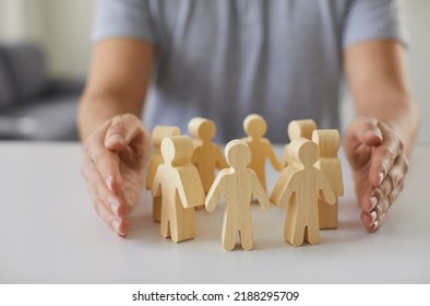 Social protection. Wooden figurines of people surrounded by man's hands symbolizing care for employees, customers or family. Close-up of figurines of people standing in circle on table and male - Shutterstock ID 2188295709