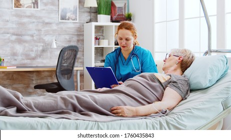 Social worker consulting an elderly disabled woman who lies in hospital bed. The caregiver uses a clipboard to take pensioners notes
